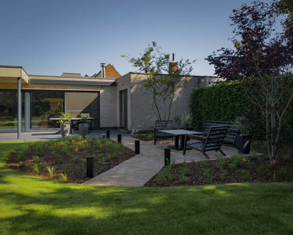 Moderne tuin met een groot functioneel terras tegen de woning en een loungeterras temidden van prairiebeplanting met siergrassen, gerealiseerd in Sint-Niklaas