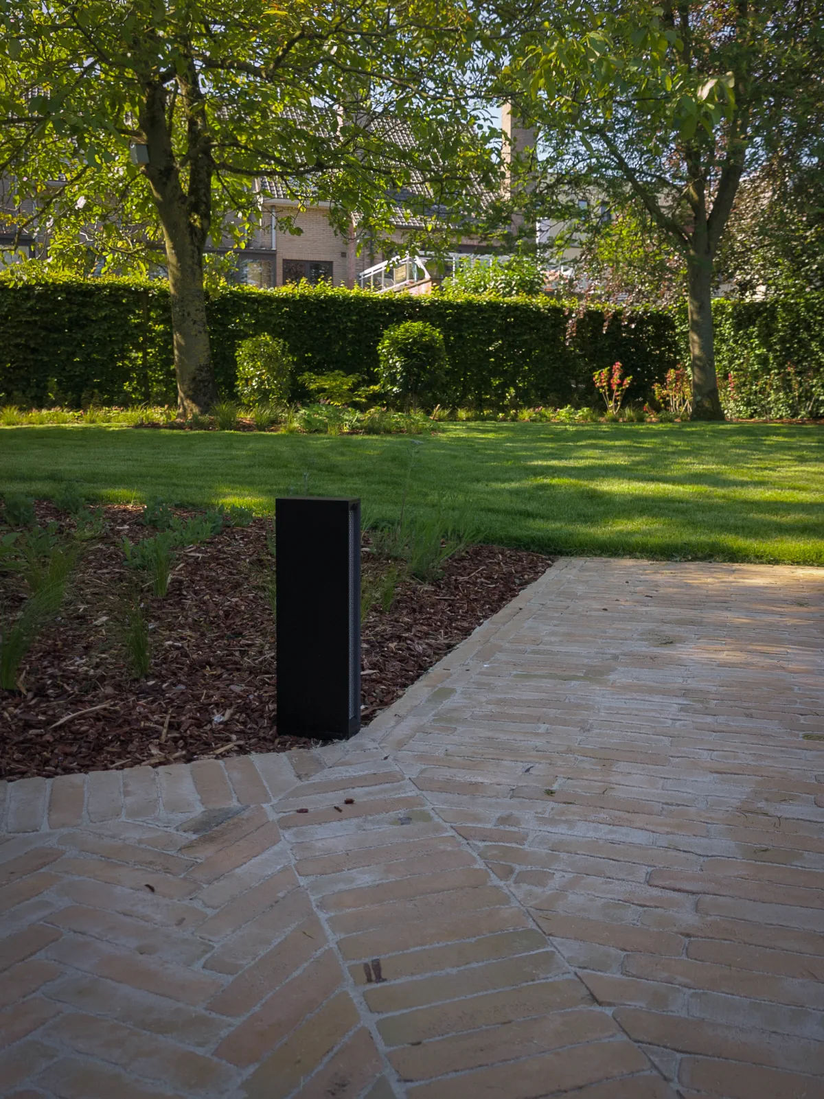 modern tuinpad in beige klinkers in een plantenborder met tuinverlichting, gerealiseerd in Sint-Niklaas