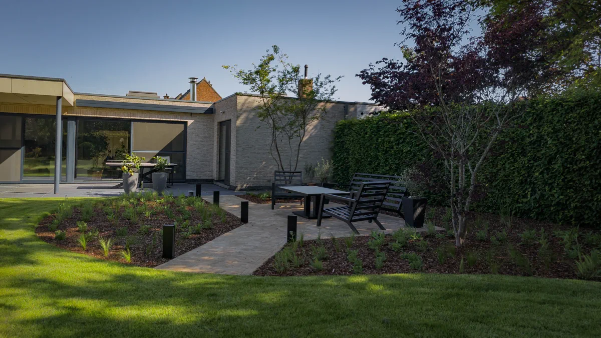 Moderne tuin met een groot functioneel terras tegen de woning en een loungeterras temidden van prairiebeplanting met siergrassen, gerealiseerd in Sint-Niklaas